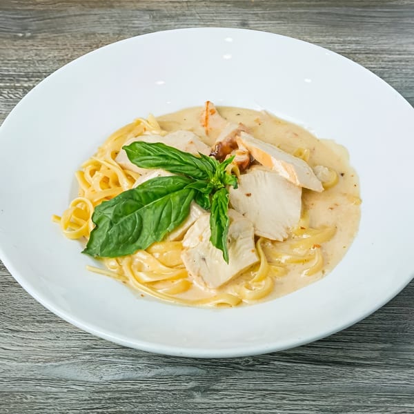 Creamy chicken fettuccine alfredo with fresh basil on a white plate from Canadian Pizza & Grill.