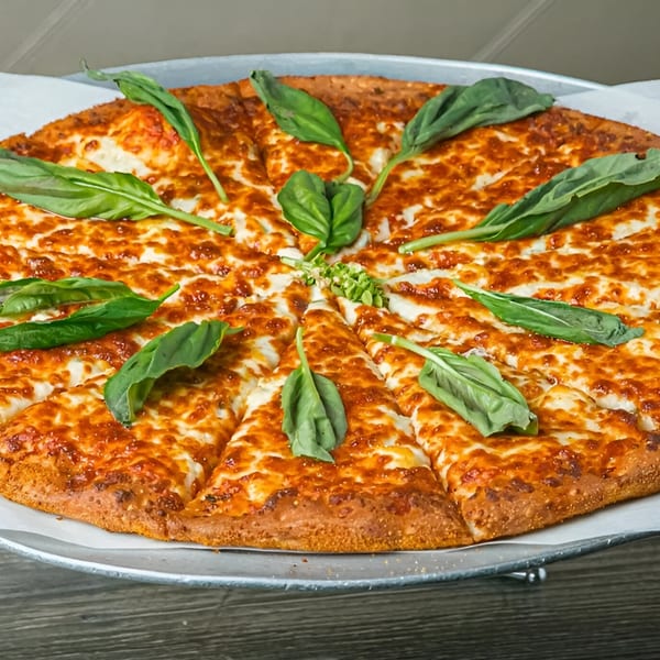 A freshly baked Canadian Pizza & Grill cheese pizza, garnished with basil leaves, on a metal tray.