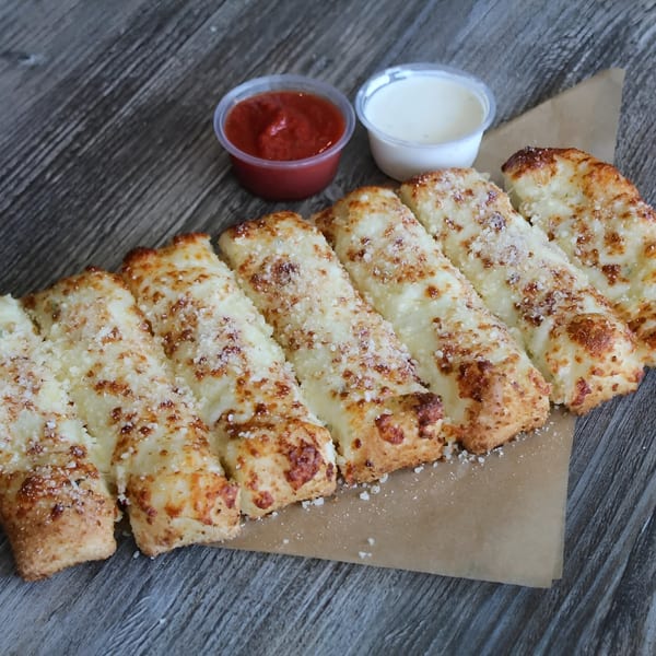 Cheesy garlic breadsticks with parmesan, served with marinara and ranch dipping sauces on wood.