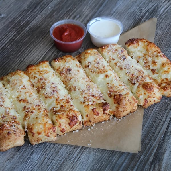 Cheesy breadsticks with parmesan, served with marinara and ranch dipping sauces on a wooden table.