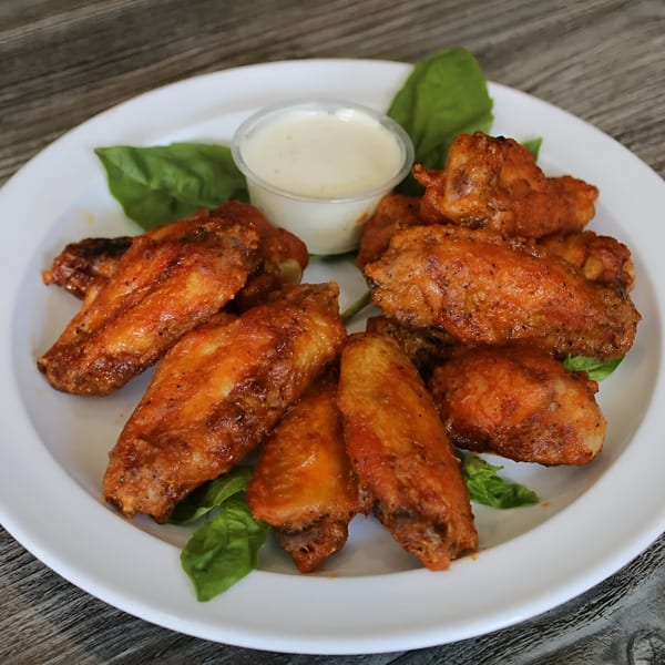 A plate of Canadian Pizza & Grill's crispy chicken wings with a side of ranch dressing.