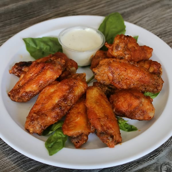 A plate of Canadian Pizza & Grill's spicy chicken wings with a side of dipping sauce.