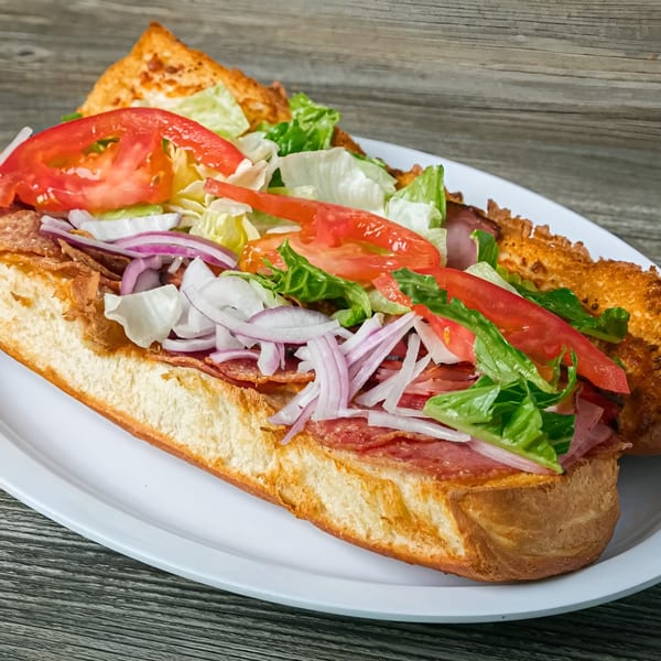 A Canadian Pizza & Grill submarine sandwich, loaded with meats, lettuce, tomatoes, and onions on a white plate.