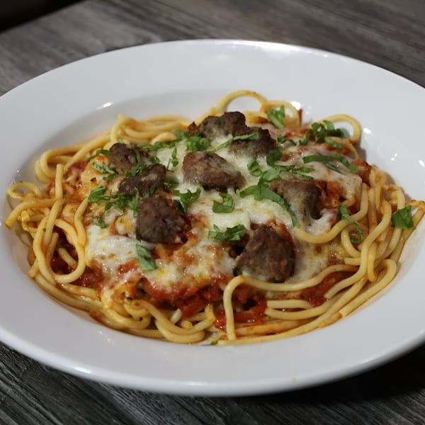 Spaghetti with meatballs, melted mozzarella cheese, and fresh basil in a white bowl.