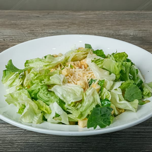 Fresh Caesar salad with crisp lettuce, croutons, and shredded Parmesan cheese in a white bowl.